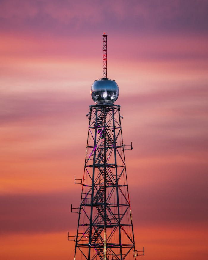 A prominent communications tower stands silhouetted against a vibrant sunset sky, showcasing modern telecommunication technology.